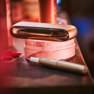 IQOS 3 DUO w kolorze Brilliant gold z wkładem tytonowym HEETS leżący na czerwonym notatniku