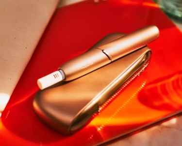 IQOS 3 DUO w kolorze Brilliant gold z wkładem tytonowym HEETS leżący na czerwonym notatniku