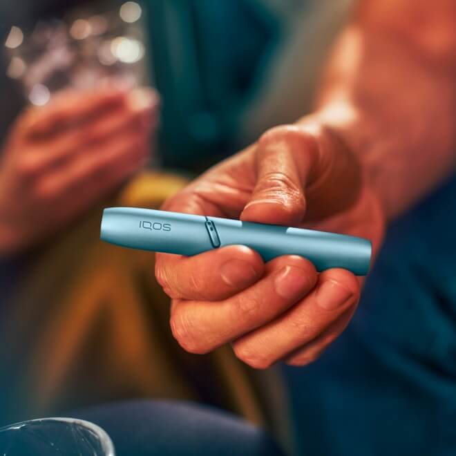 Podgrzewacz IQOS Originals DUO w kolorze turkusowym trzymany w dłoni.