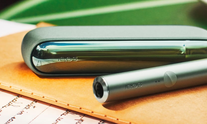 Podgrzewacz IQOS ILUMa w kolorze Moss Green leżący na notesie