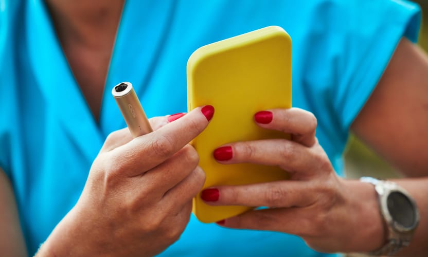 Podgrzewacz IQOS ILUMA I telefon komórkowy w dłoniach