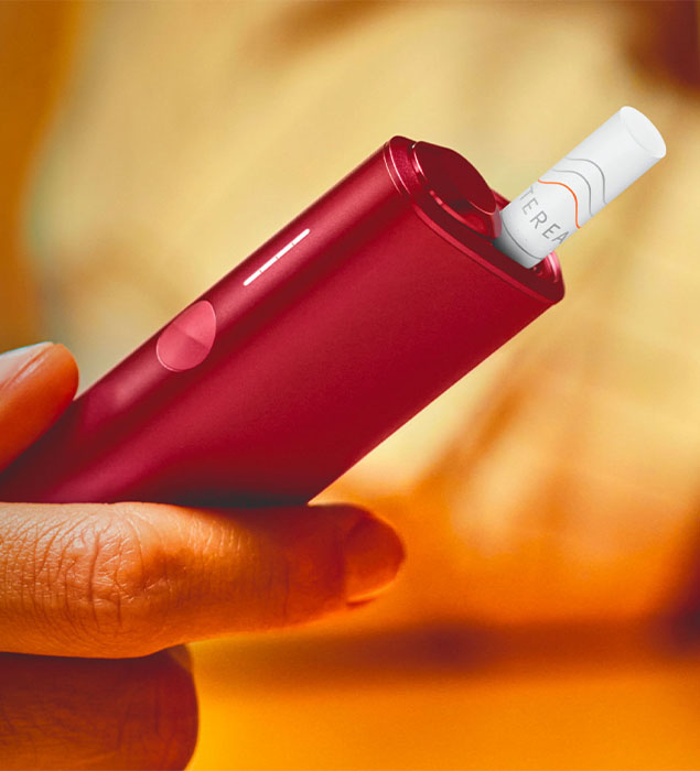 Podgrzewacz IQOS ILUMA w kolorze Sunset Red z wsuniętym wkładem tytoniowym trzymany w dłoni