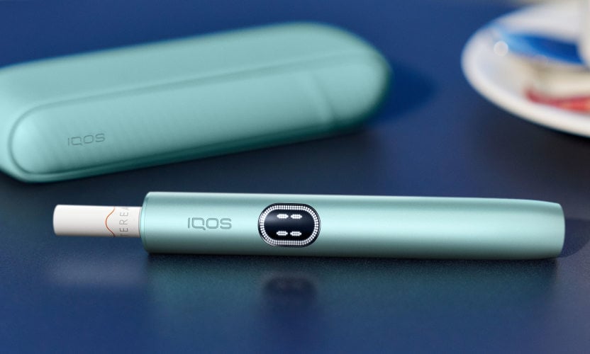 Podgrzewacz IQOS ILUMA i z włożónym wkładem tytoniowym leżący obok przenośnej ładowarki
