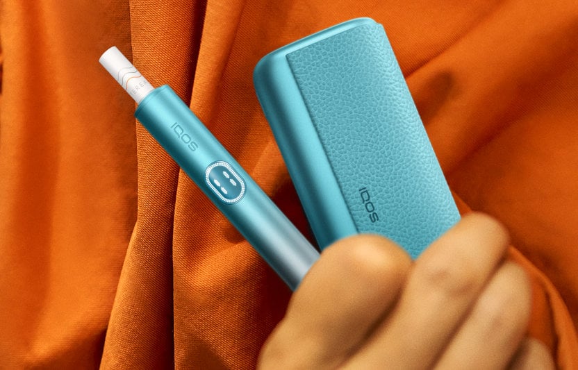 Podgrzewacz IQOS ILUMA i PRIME z włożonym wkładem tytoniowym i przenośna ładowarka trzymane w dłoni