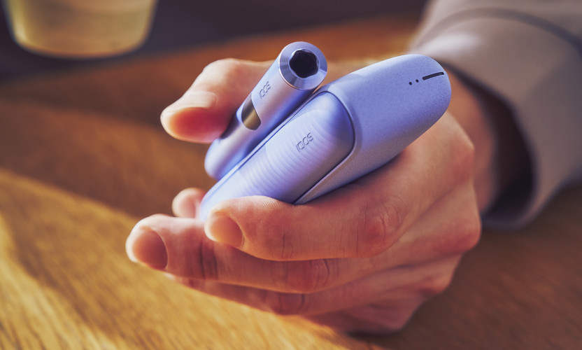 IQOS ILUMA i w fioletowym kolorze w dłoni osoby siedzącej z kubkiem
