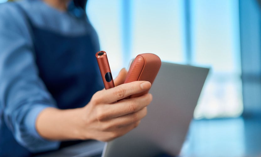 Podgrzewacz IQOS ILUMA i z przenośną ładowarką trzymane w dłoni