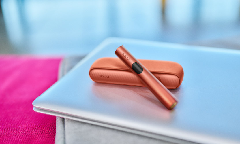Podgrzewacz IQOS ILUMA i z przenośną ładowarką w czerwony odcieniu leżące na zamkniętym laptopie