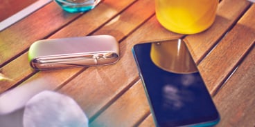 Gold IQOS DUO with a mobile, a glass of water and a yellow cup on a wooden table