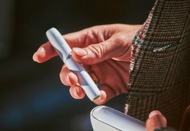 Person's hands holding a white IQOS 3 DUO in one, the charger in the other