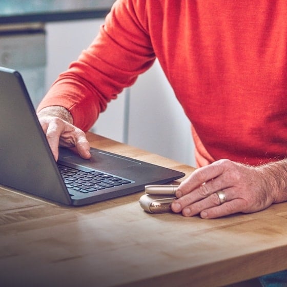 Man working at laptop, one hand on IQOS device on table