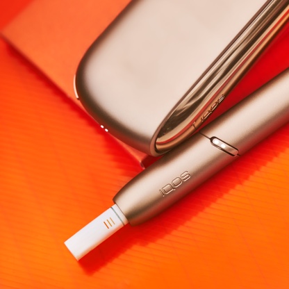 Podgrzewacz IQOS z wkładem tytoniowym HEETS obok przenośnej ładowarki leżącej na czerwonym notatniku