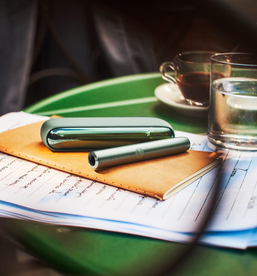 Podgrzewacz IQOS ILUMA w kolorze Moss Green leżący na notesie
