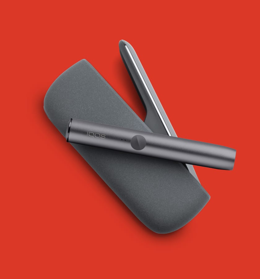 Podgrzewacz IQOS ILUMA leżący na przenośnej ładowarce na czerwonym tle