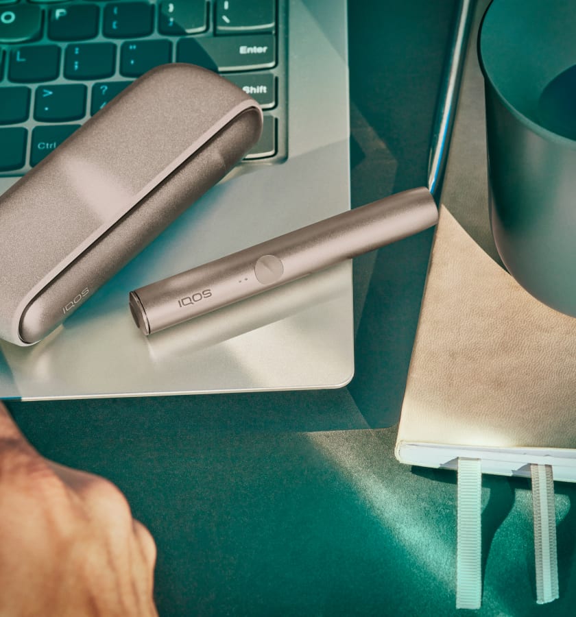 Podgrzewacz i przenośna ładowarka IQOS ILUMA leżące na otwartym laptopie