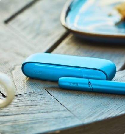 Podgrzewacz oraz przenośna ładowarka IQOS ORIGINALS DUO leżące obok siebie na stoliku