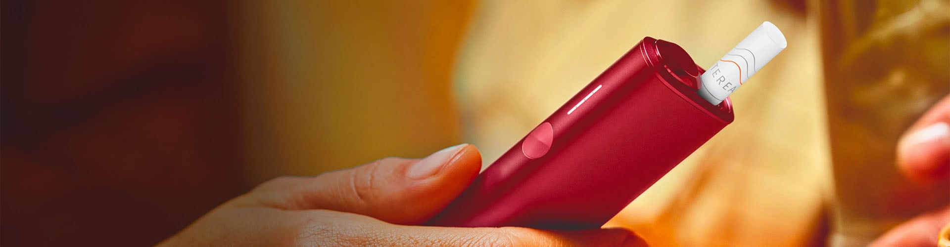 Podgrzewacz IQOS ILUMA w kolorze Sunset Red z wsuniętym wkładem tytoniowym trzymany w dłoni