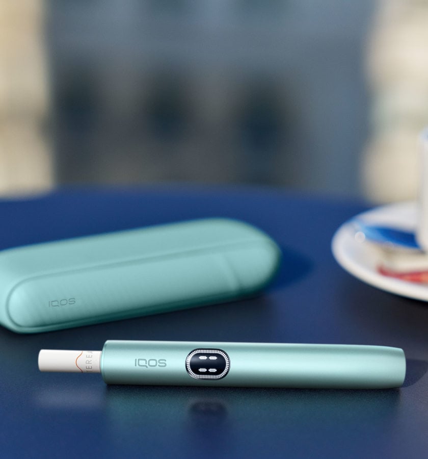 Podgrzewacz IQOS ILUMA i z włożónym wkładem tytoniowym leżący obok przenośnej ładowarki