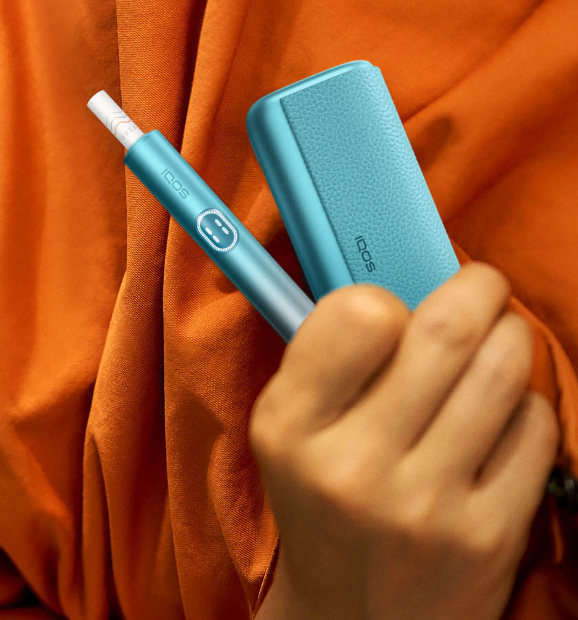 Podgrzewacz IQOS ILUMA i PRIME z włożonym wkładem tytoniowym i przenośna ładowarka trzymane w dłoni