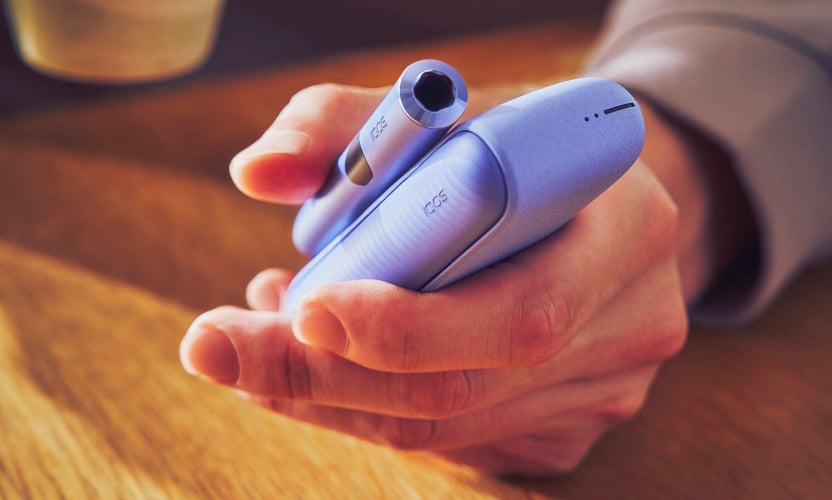 IQOS ILUMA i w fioletowym kolorze w dłoni osoby siedzącej z kubkiem