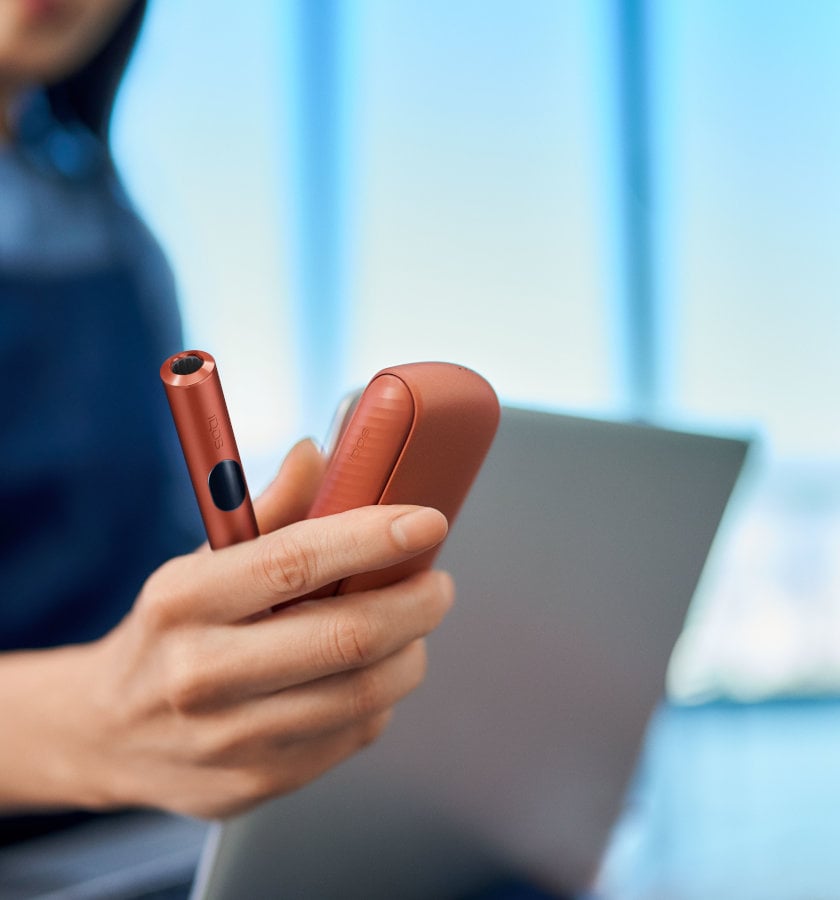 Podgrzewacz IQOS ILUMA i z przenośną ładowarką trzymane w dłoni