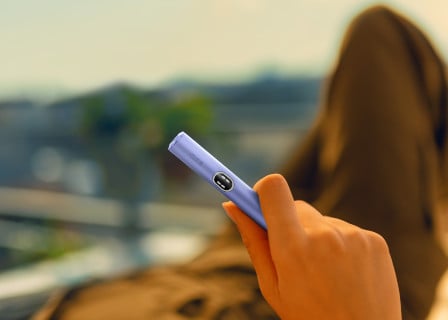 Fioletowy podgrzewacz IQOS ILUMA i z ekranem dotykowym w dloni osoby spędzającej czas na dworze.
