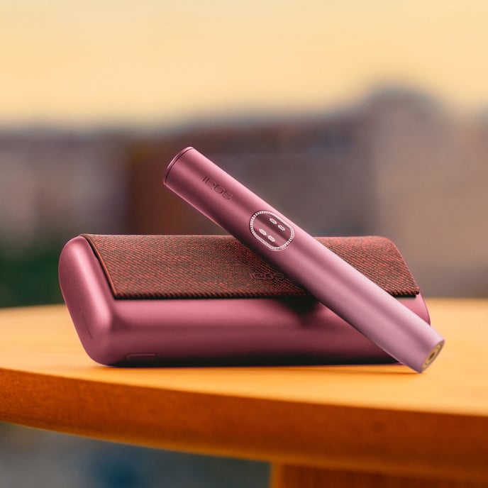 Podgrzewacz IQOS ILUMA i oparty o leżącą obok przenośną ładowarkę
