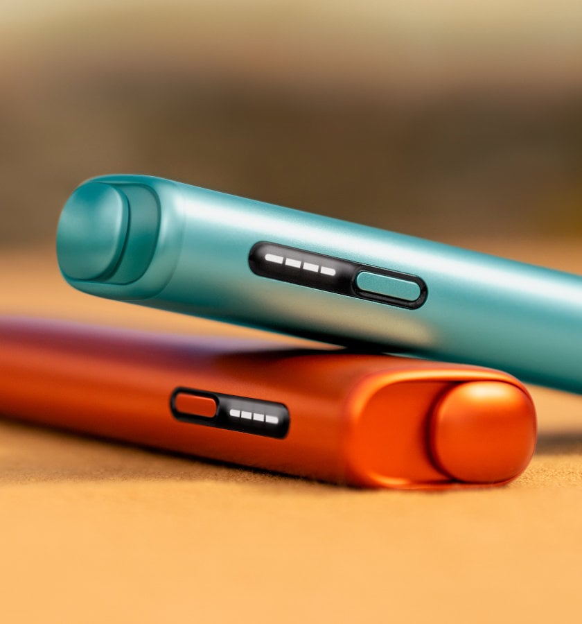 Leżące na stole czewony i niebieski podgrzewacze IQOS ILUMA i ONE