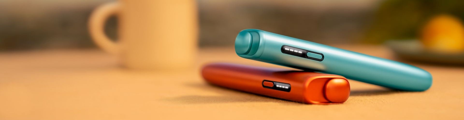 Dwa podgrzewacze IQOS ILUMA i ONE w różnych kolorach, leżące jeden na drugim