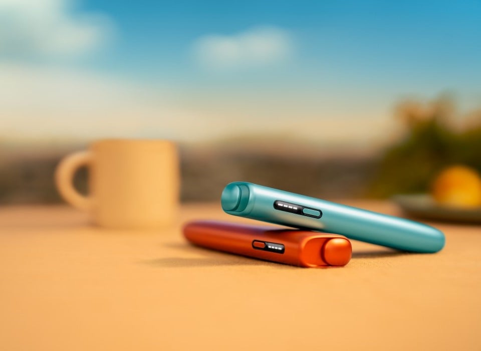 Dwa podgrzewacze IQOS ILUMA i ONE w różnych kolorach, leżące jeden na drugim