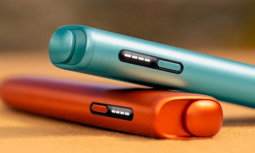 Leżące na stole czewony i niebieski podgrzewacze IQOS ILUMA i ONE