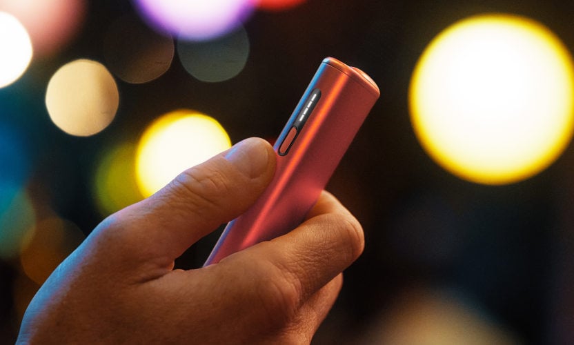 IQOS ILUMA I ONE w czerwonym odcieniu, trzymany w dłoni, w wieczornym świetle