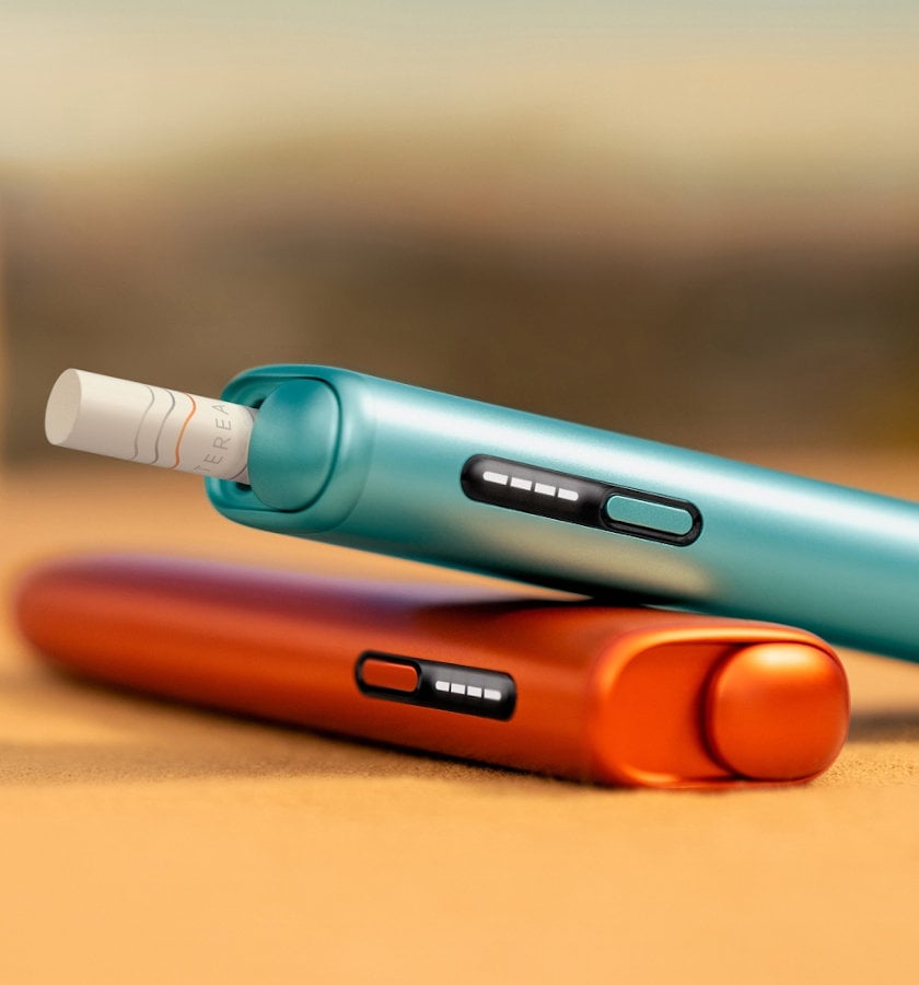 Dwa podgrzewacze IQOS ILUMA i ONE, w kolorach niebieskim i czerwonym, w jednym z podgrzewaczy włożony wkład tytoniowy