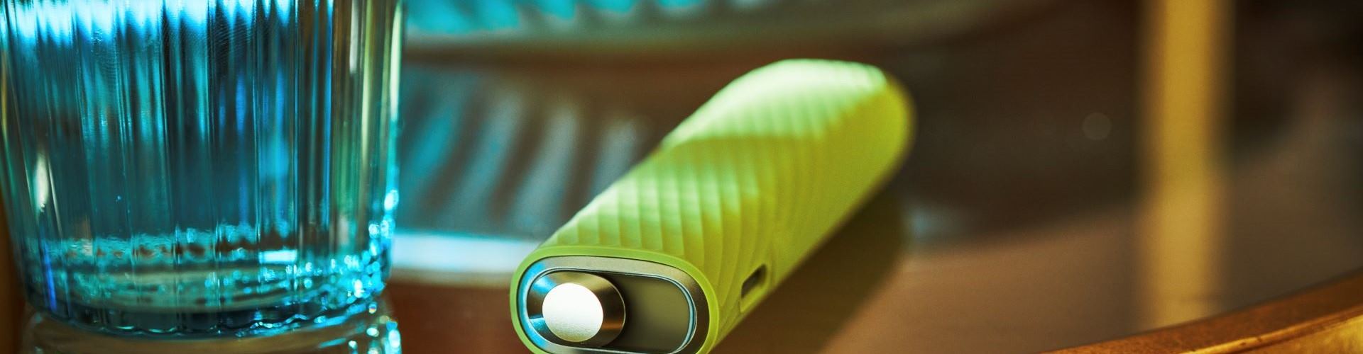 Podgrzewacz IQOS ILUMA ONE w silikonowej obudowie leżący obok szklanki z wodą
