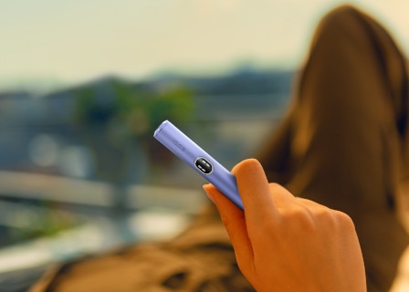 Fioletowy podgrzewacz IQOS ILUMA i z ekranem dotykowym w dloni osoby spędzającej czas na dworze.