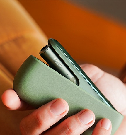 IQOS ILUMA w kolorze zielonym w dłoni. Otwara ładowarka z umieszczony w środku podgrzewaczem