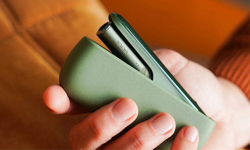 IQOS ILUMA w kolorze zielonym w dłoni. Otwara ładowarka z umieszczony w środku podgrzewaczem