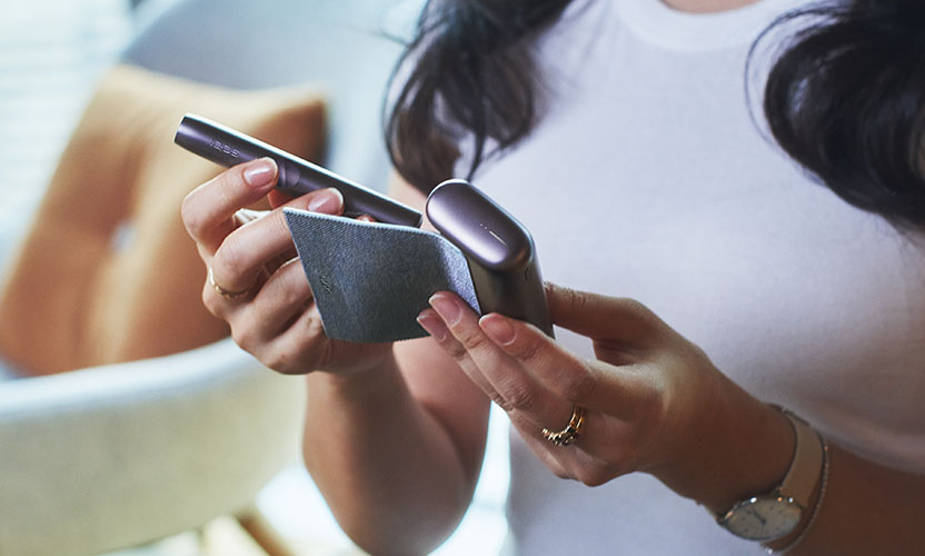 Kobieta wyjmuje podgrzewacz IQOS ILUMA PRIME z ładowarki. Urządzenie w kolorze beżowym