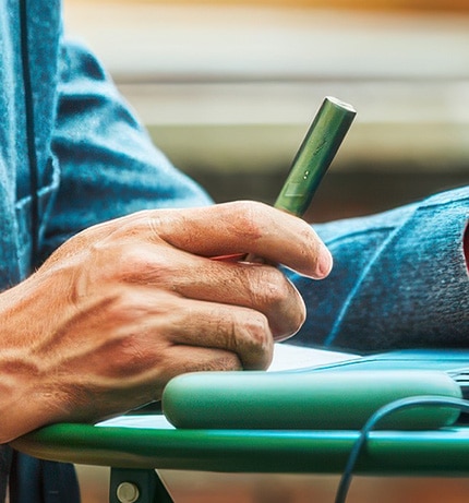 Mężczyzna korzysta z laptopa. W dłoni trzyma zielony podgrzewacz IQOS ILUMA
