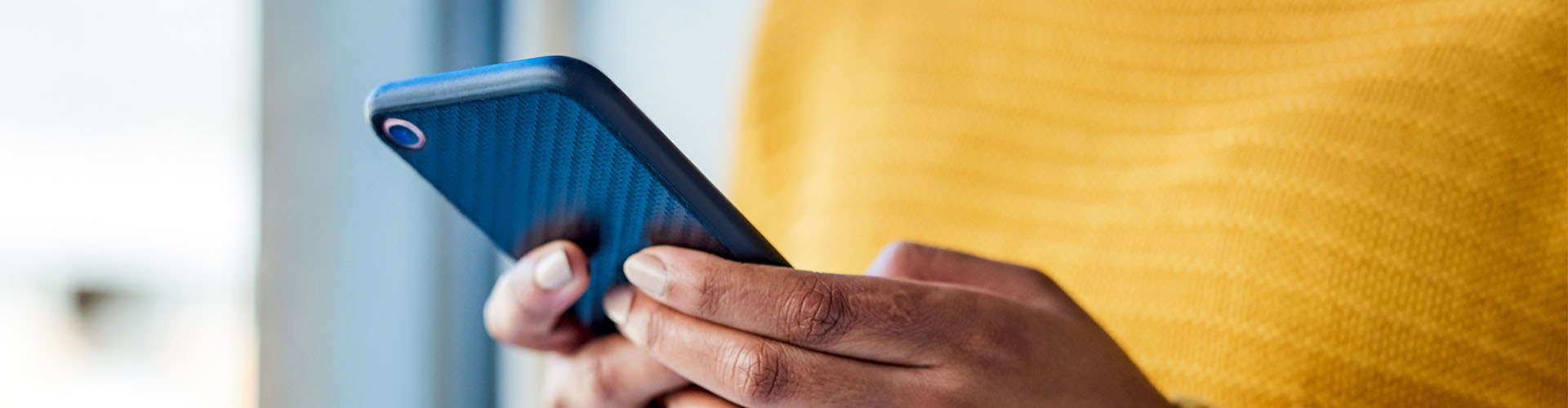 Osoba w żółtym swetrze trzymająca telefon w dłoniach