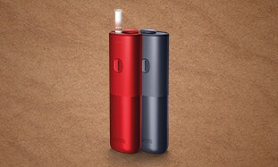 Stojące obok siebie podgrzewacze BONDS by IQOS, czerwony i czarny, w jednym wsunięty wkład tytoniowy BLENDS