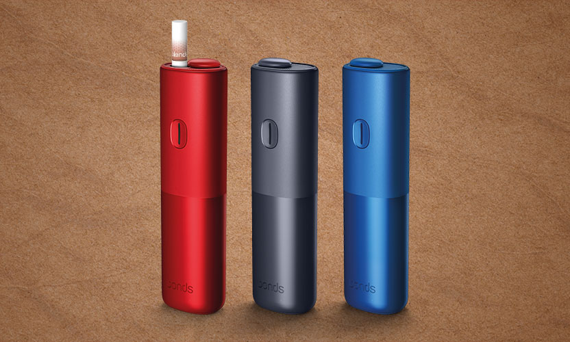 Stojące obok siebie podgrzewacze BONDS by IQOS, czerwony, czarny i niebieski, w jednym wsunięty wkład tytoniowy BLENDS