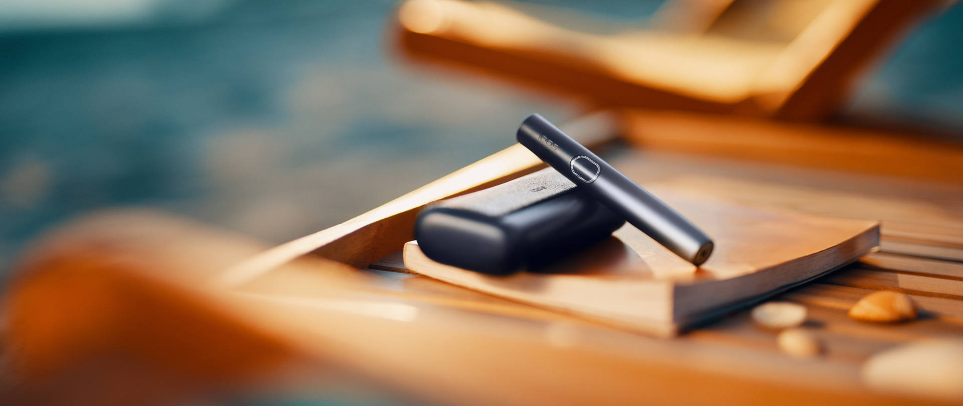 Podgrzewacz tytoniu IQOS ILUMA i PRIME w kolorze czarnym ułożony na książce, na drewnianym leżaku