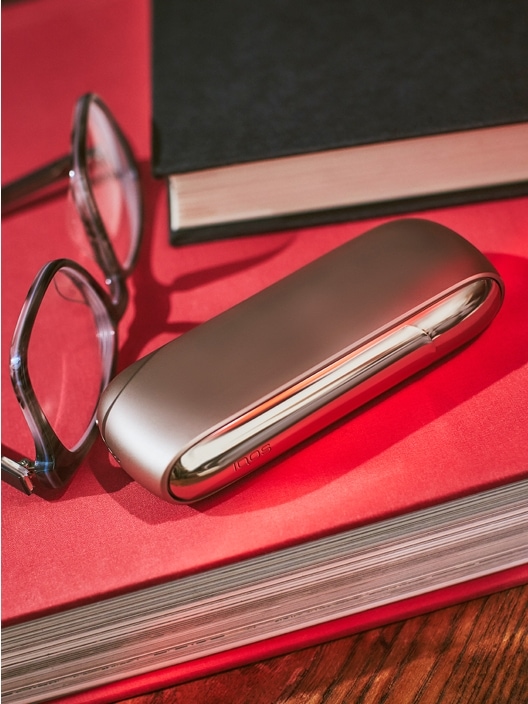 IQOS 3 DUO charger next to book and glasses
