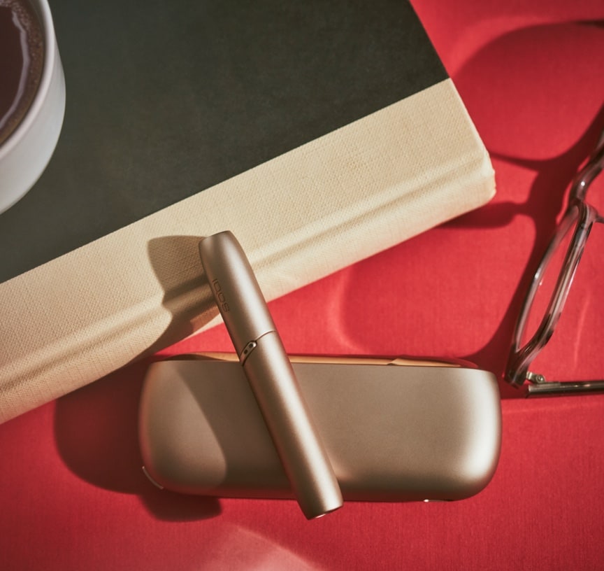 A gold IQOS device resting on a book.