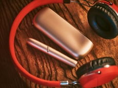 IQOS 3 DUO and charger on table alongside red headphones