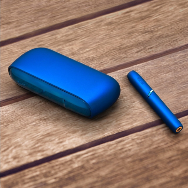 A blue IQOS device and holder on a wooden surface.