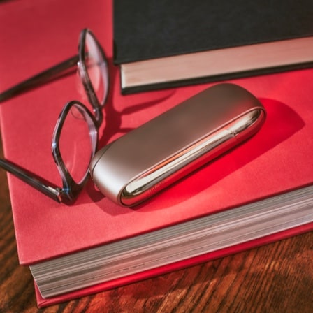 A gold IQOS device next to a pair of spectacles.