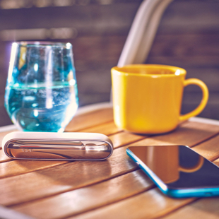 Gold IQOS DUO on a wooden table with a glass of water and a yellow cup