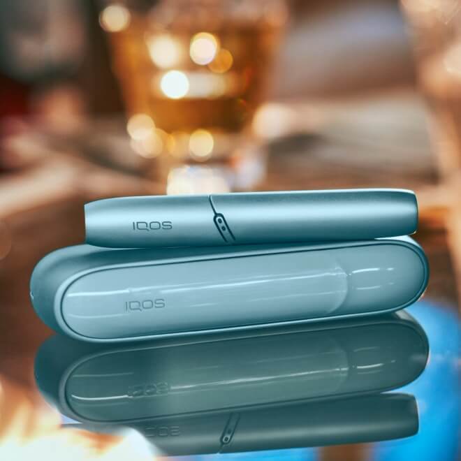 Turquoise IQOS Originals Duo device on a shiny coffee table.