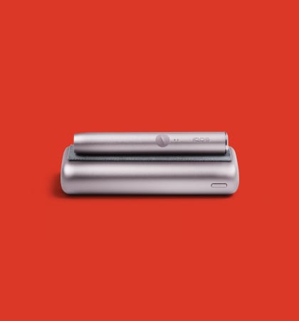 IQOS ILUMA PRIME holder lying on a pockete charger on a red background